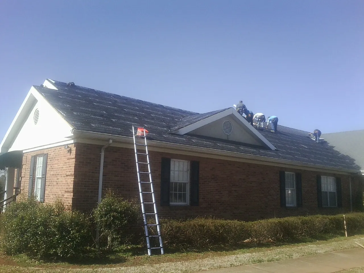 Crew tearing shingles off a brick ranch roof with a ladder set — Emergency Roof Repair work by our crew in Itasca