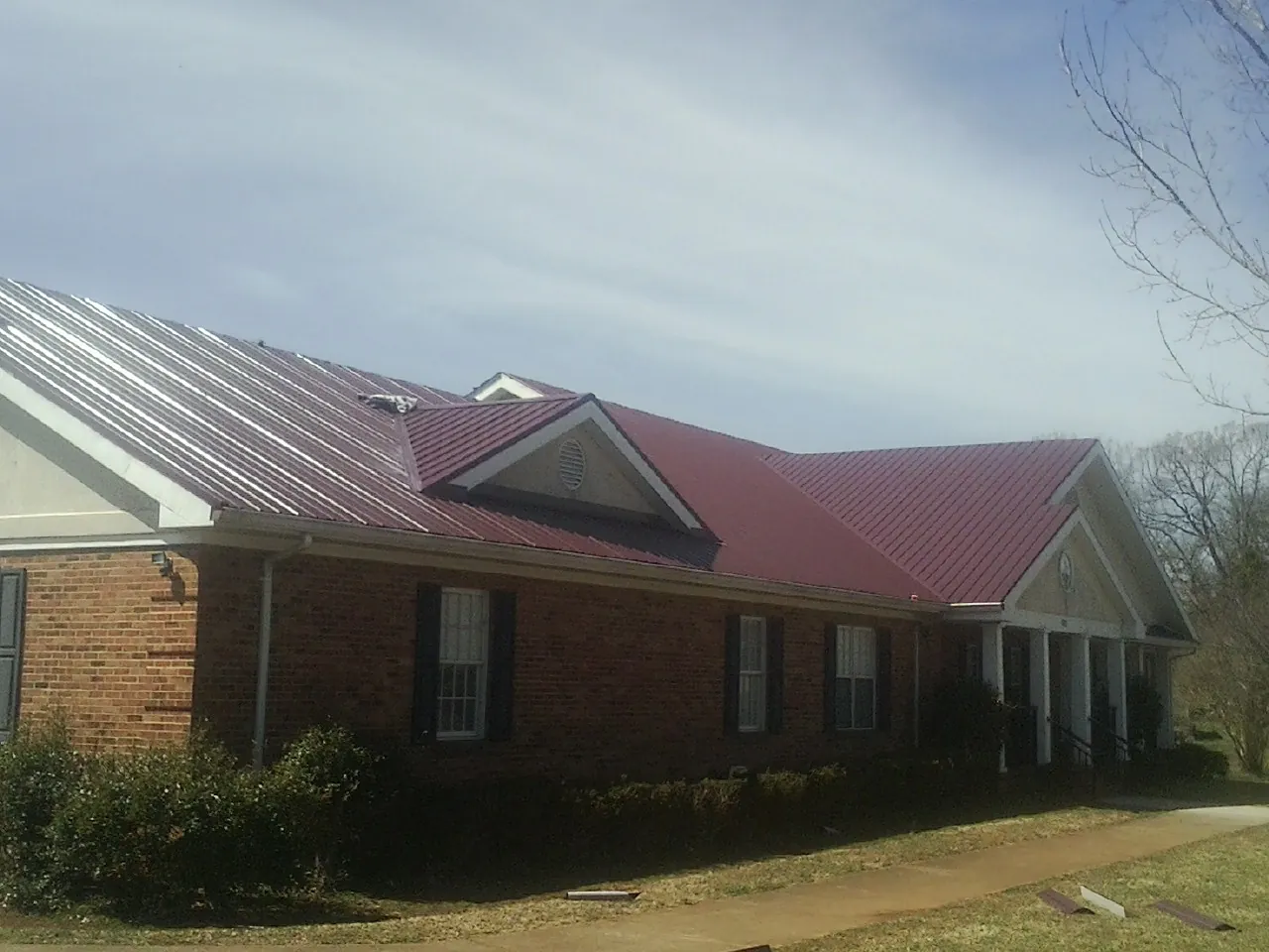 Red metal roof with gabled entries on a long brick building, from a Hail Damage Roof Repair job in Itasca