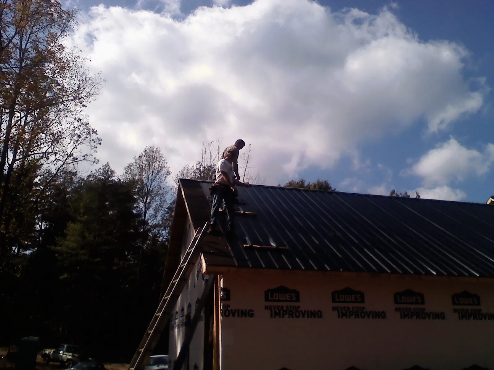 Roofer fastening dark metal panels high against a cloudy sky, from a Roof Inspection job in Itasca