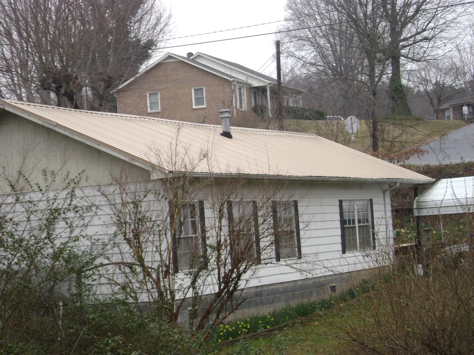 Tan metal roof on a white sided house set into a hillside — Commercial Roofing by Roofing Brothers in Itasca